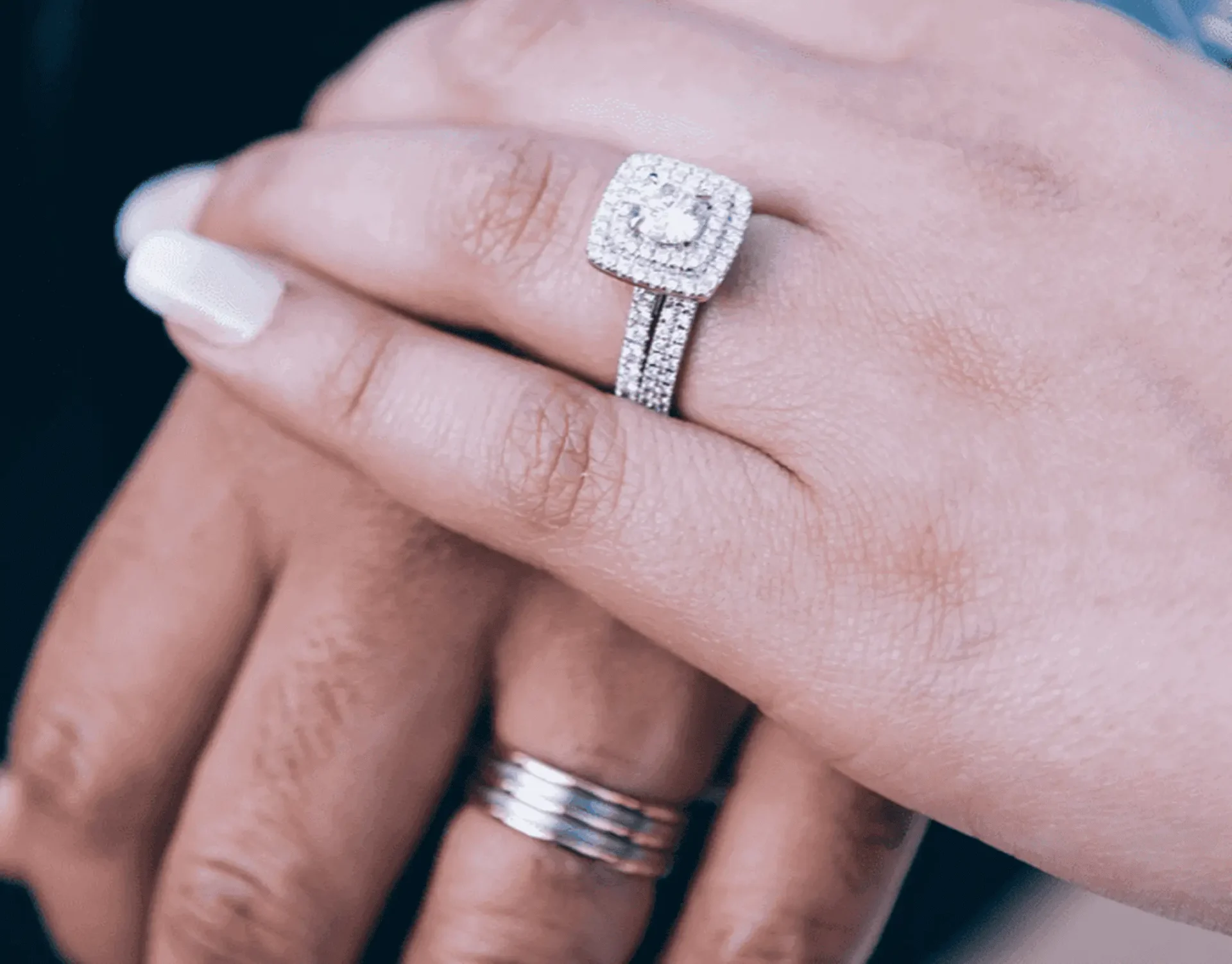 Couple's hands showing diamond engagement and wedding rings